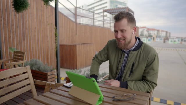 Young-man-is-communicating-by-internet-call-through-tablet-sitting-outdoors