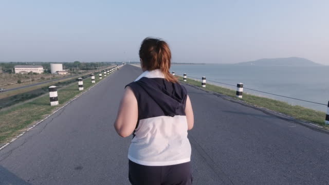 Asiatische-Frauen-joggen-in-der-Straße-am-frühen-Morgen-Sonnenlicht-am-Wasserspeicher-Pa-Sak-Jolasid-Dam.-Konzept-des-Gewichtsverlustes-mit-Bewegung-für-die-Gesundheit.-Blick-nach-dem-Blick