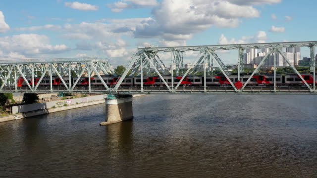 Luftaufnahme-der-Eisenbahnbrücke,-mit-einem-fahrenden-Zug-auf-ihr,-über-den-Fluss,-der-durch-eine-Großstadt-fließt