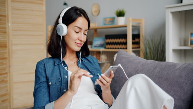 Slow-motion-of-pretty-girl-listening-to-music-in-headphones-using-smartphone
