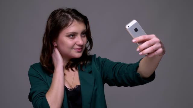 Nahaufnahme-Shooting-von-Erwachsenen-attraktiv-Brünette-weiblich,-die-Selfies-auf-dem-Handy-mit-Hintergrund-isoliert-auf-grau
