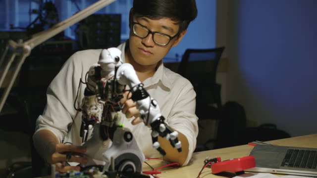 Jóvenes-ingenieros-de-desarrollo-de-electrónica-asiática-construyendo,-probando,-arreglando-robótica-en-el-laboratorio-de-investigación-en-ciencias-de-la-computación-por-la-noche.-Personas-con-concepto-de-tecnología-o-innovación.