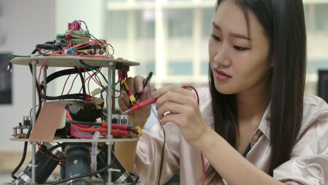 La-ingeniera-de-electrónica-asiática-trabaja-con-robots,-construyendo,-arreglando-robótica-en-taller.-Personas-con-concepto-de-tecnología-o-innovación.