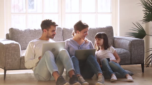 Glückliche-moderne-Familie-sitzen-auf-dem-Boden-sprechen-mit-Geräten