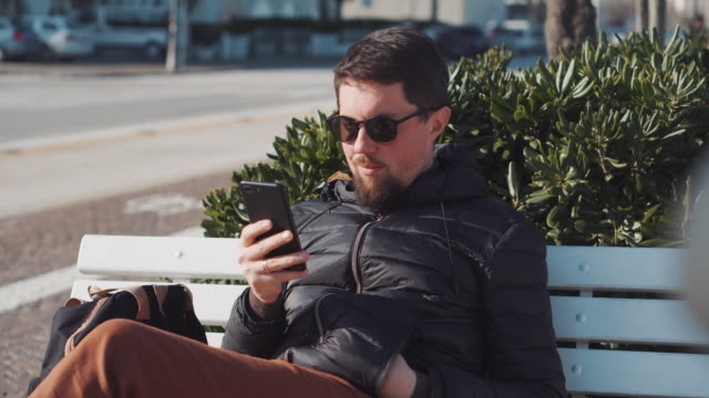 Man-is-browsing-by-smartphone-sitting-outdoors