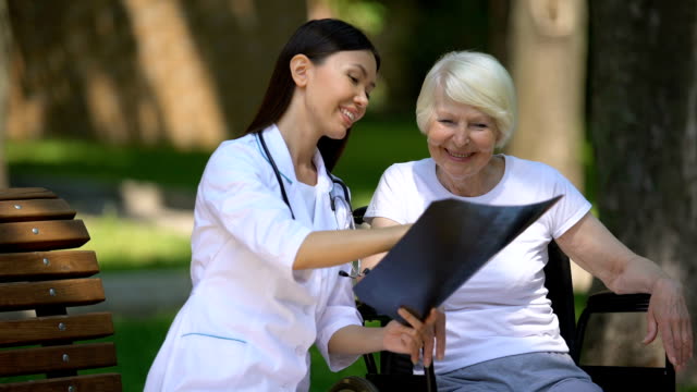 Lächelnde-Ärztin-zeigt-radfahrerfreundliche-ältere-Frau-im-Rollstuhl