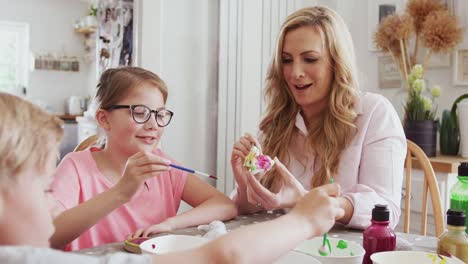 Family-sitting-around-kitchen-table-with-parents-helping-children-to-paint-Easter-decorations---shot-in-slow-motion