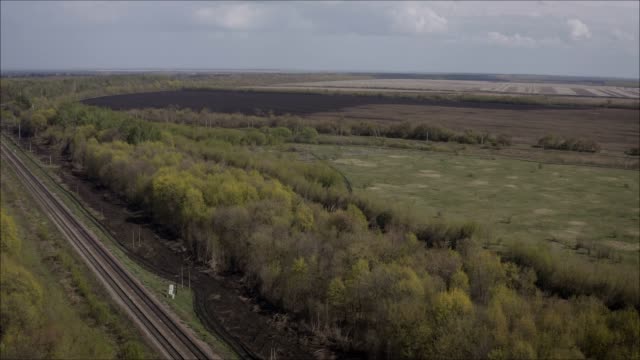 A-railway-track-passing-through-the-forest-and-field.-Shooting-from-a-height.-Russian-railway,-taken-from-a-height.