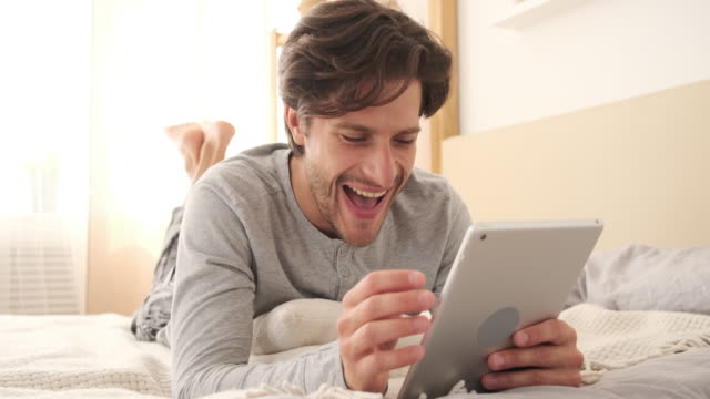 Hombre-divirtiéndose-usando-la-tableta-digital-en-la-cama