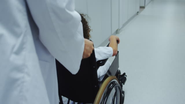 Nahaufnahme-von-kaukasischen-männlichen-Arzt-schieben-schieben-afrikanischen-amerikanischen-Jungen-im-Rollstuhl-im-Krankenhaus-4k