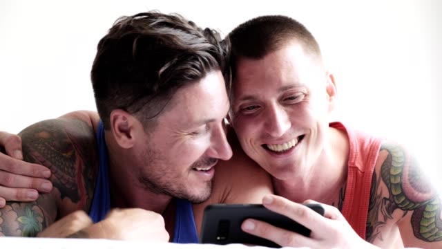 Schwules-Paar-im-Bett-mit-Telefon.-Video-rufen-ihre-Freunde.