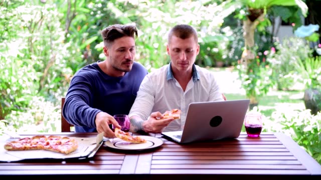 Gay-couple-having-pizza-for-lunch.-Typing-and-looking-at-screen.