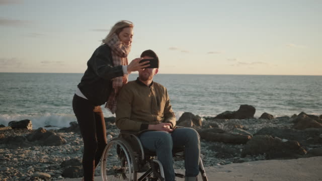 Männlicher-Rollstuhlfahrer-und-seine-Freundin-machen-Selfie-per-Smartphone