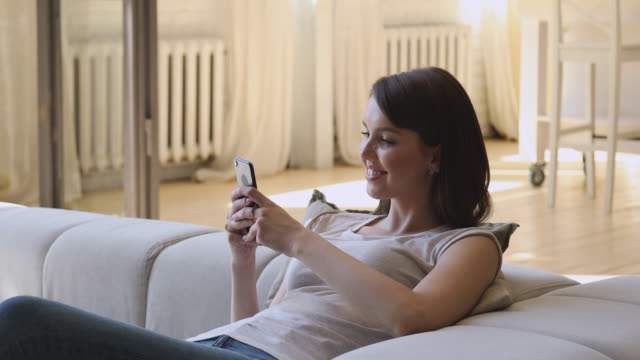 Lächelnd-entspannte-junge-Frau-hält-Smartphone-SMS-zu-Hause
