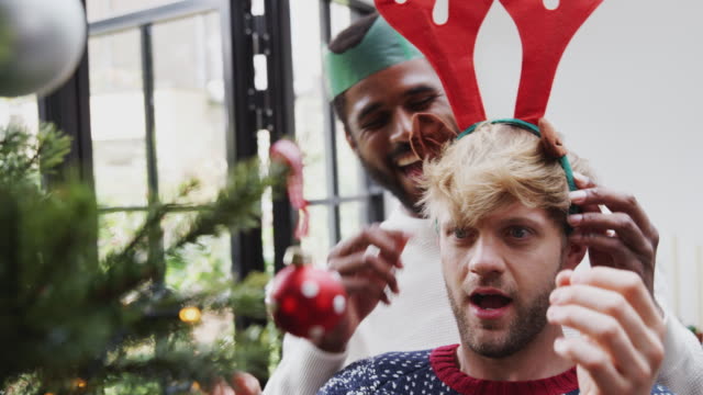 Hombre-poniendo-astas-de-vestir-de-lujo-en-pareja-masculina-mientras-cuelgan-decoraciones-en-el-árbol-de-Navidad-juntos