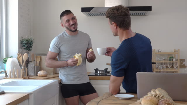 Gay-male-couple-talking-and-laughing-in-kitchen-at-breakfast-time