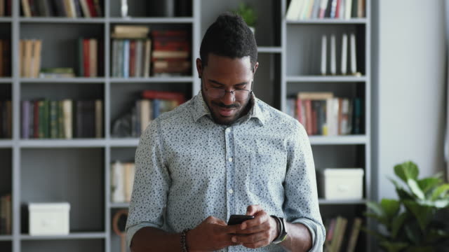 Hombre-de-negocios-africano-sonriente-usando-teléfono-inteligente-de-pie-en-la-oficina