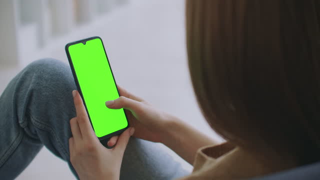 Point-of-View-of-Woman-at-Modern-Room-Sitting-on-a-Chair-Using-Phone-With-Green-Mock-up-Screen-Chroma-Key-Surfing-Internet-Watching-Content-Videos-Blogs-Tapping-on-Center-Screen