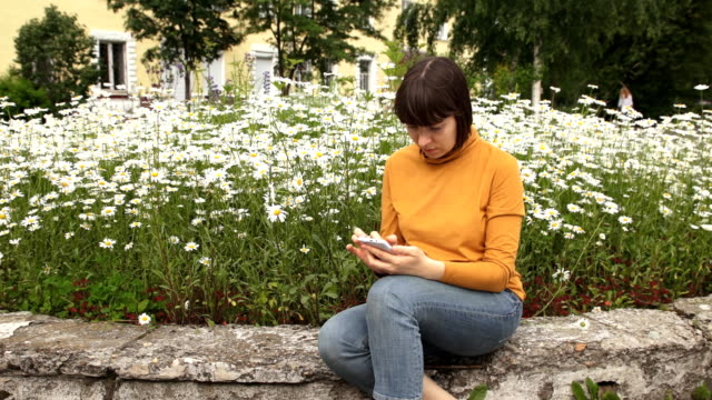 A-brunette-in-a-yellow-turtleneck-uses-a-phone-sitting-next-to-camomiles