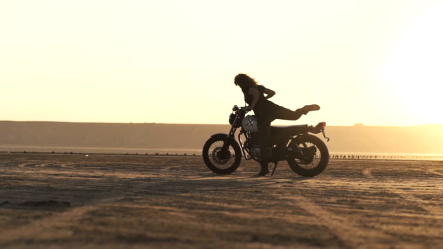 Junge-schöne-Frau-geht-an-ihr-altes-Café-Racer-Motorrad,-sitzt-auf-ihm-und-macht-einen-Burnout,-dann-reitet-entfernt.-Weibliche-Motorradfahrer.