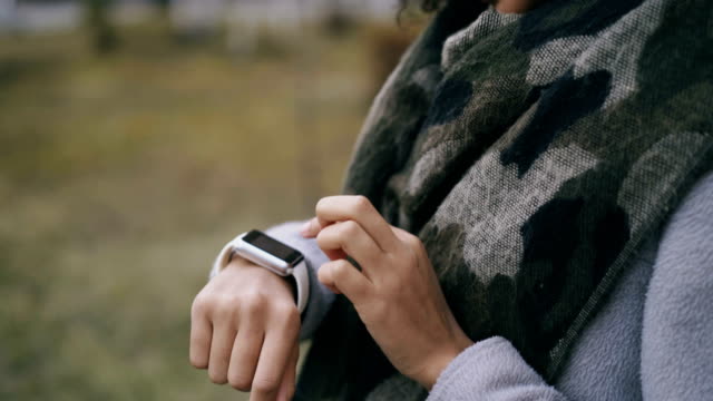 Closeup-tilt-up-shot-of-mixed-race-student-girl-using-smartwatch-and-smiling-near-univercity