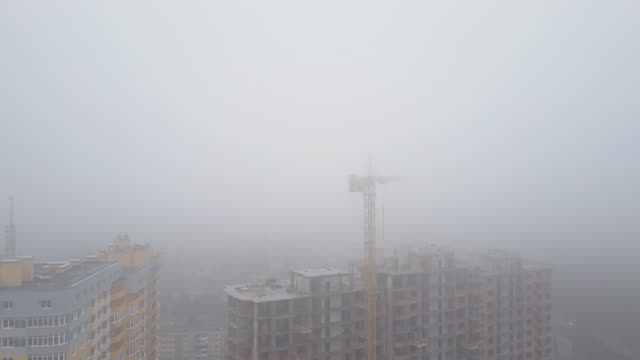 Aerial-view.-A-multi-storey-brick-house-in-the-city-in-a-fog.-A-construction-crane-is-installed-on-the-site-of-the-construction-of-a-residential-building.-New-homes-for-sale-and-rent-of-real-estate