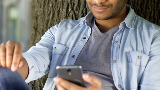 Handsome-biracial-man-smiling-and-chatting-in-social-media,-using-smartphone
