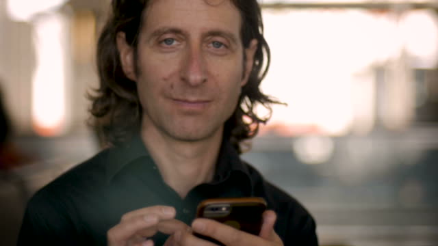 Mann-in-seinem-30er-oder-40er-Jahren-mit-Smartphone-Look-up-an-Kamera-und-lächelt