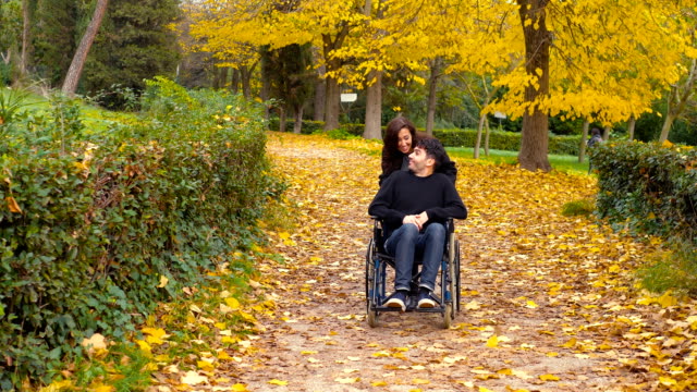 glückliche-Frau-schiebt-ihr-Freund-im-Rollstuhl-in-den-Park-in-ein-Herbsttag