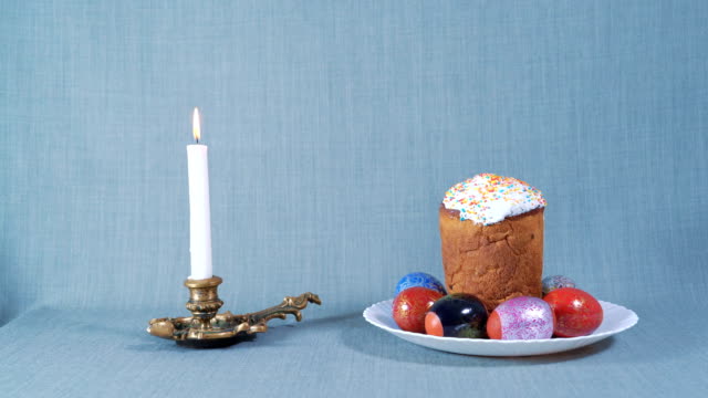 Arrival-Cameras,-Easter-Arrangement,-Easter-in-the-White-Plate-with-Dyed-Eggs,-Nearby-Burning-White-Candle