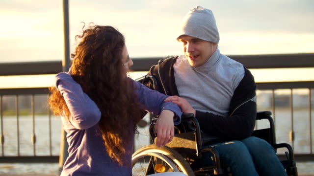 Glückliches-Paar---behinderte-Menschen-im-Rollstuhl-im-Gespräch-mit-attraktiven-jungen-Frau-Enjoing-den-Sonnenuntergang