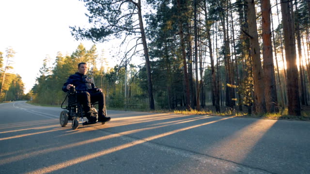 Hombre-parapléjico-se-está-moviendo-a-lo-largo-de-la-carretera-en-su-sillón-de-ruedas-accionado-en-el-bosque