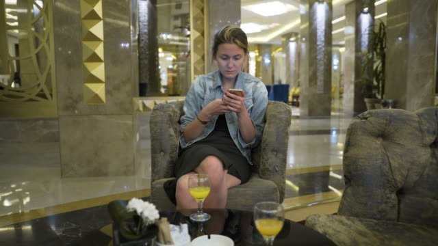 Kaukasische-Mädchen-in-eine-Jeansjacke-eine-Smartphone-nutzt,-schreibt-Nachrichten-auf-social-Network.-Sitzt-am-Tisch-im-Restaurant-Hotels