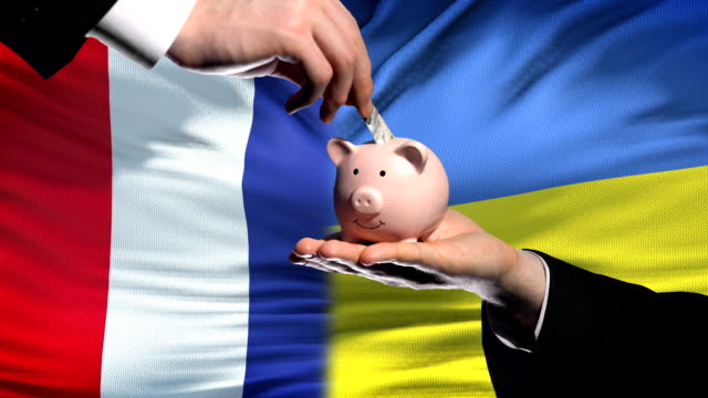 France-investment-in-Ukraine,-hand-putting-money-in-piggybank-on-flag-background