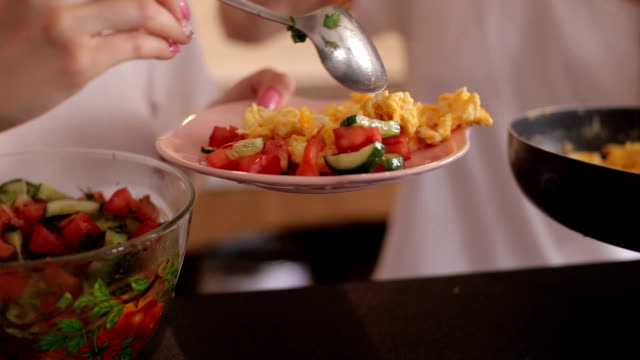 Two-girls-impose-an-omelet-and-vegetable-salad-in-a-plate,-close-up.