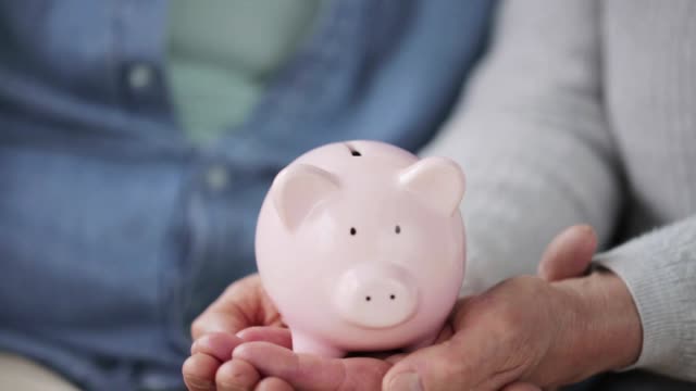 senior-couple-hands-with-coin-and-piggy-bank