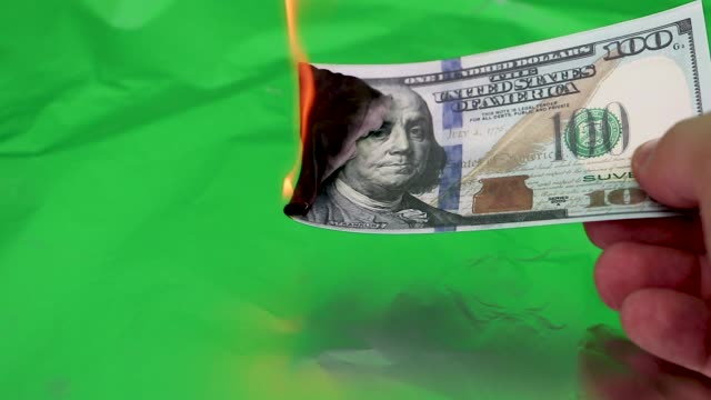 100-dollars-burning-on-a-green-background.-Concept-of-downturn-in-economy-and-loss