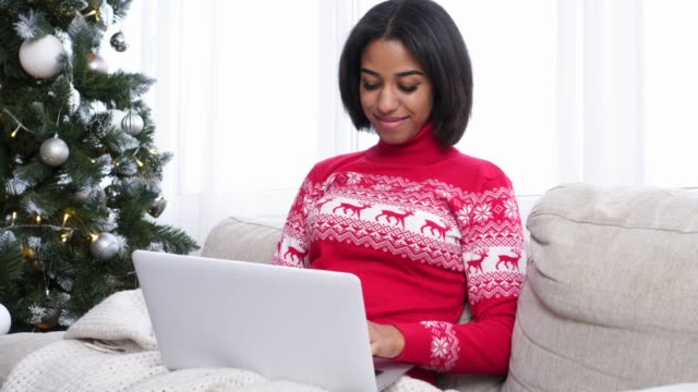 Teenager-Mädchen-mit-Laptop-auf-dem-Sofa-neben-Weihnachtsbaum-zu-Hause