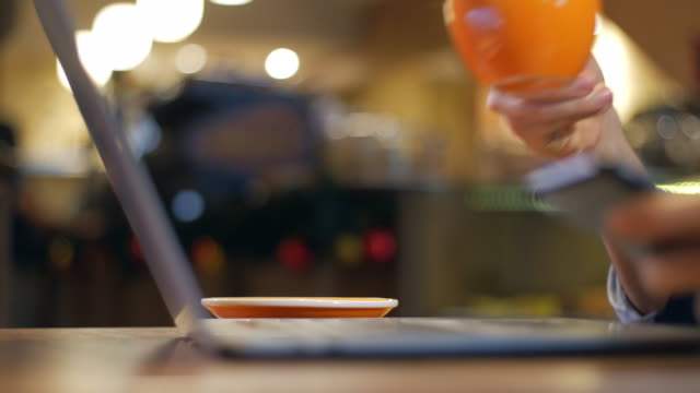 Primer-plano-del-ordenador-portátil-y-un-hombre-usando-un-teléfono-inteligente-y-tomando-café-en-una-cafetería