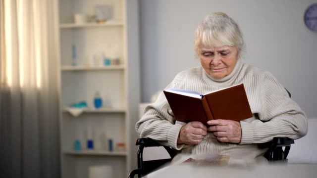 Alte-Frau-sitzt-im-Rollstuhl,-Buch-zu-lesen,-Suche-Brillen,-schlechte-Sicht