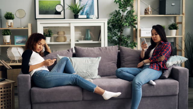 Schöne-Mädchen-Schüler-nutzen-Smartphones-mit-Gadgets-und-berührende-Bildschirme,-die-auf-Sofa-in-der-Wohnung-sitzen.-Technologien,-Menschen-und-Innenraumkonzept.