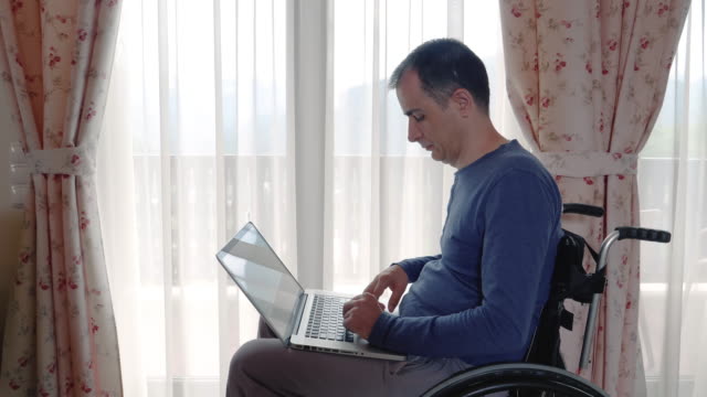 Young-man-in-wheelchair-working-at-laptop-computer-at-home
