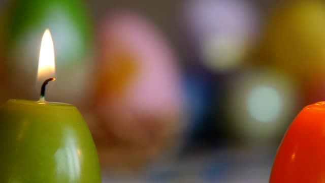 Candles-made-in-shape-of-easter-egg.-Burning-candles.-Green,-orange,-yellow.-Sliding,-close-up.