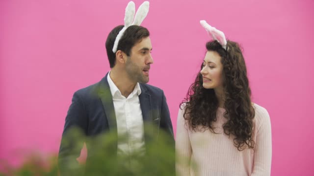 Young-couple-are-beautiful-on-pink-background.-During-this-time,-they-are-dressed-in-rabble-ears.-Looking-at-each-other,-behave-like-rabbits,-reproducing-movements-of-the-mouth-and-teeth.