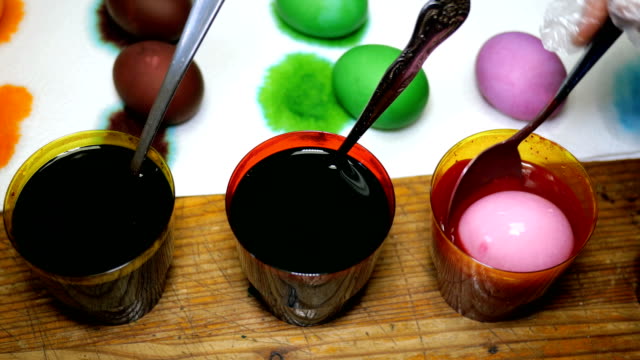 Woman-paints-Easter-eggs-in-different-colors,-dipping-them-into-cups-with-multicolored-dyes.
