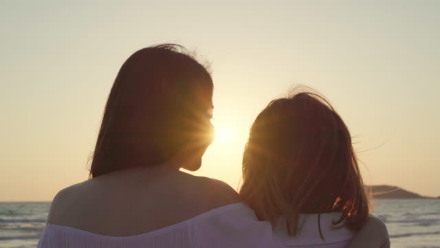 Young-Asian-lesbian-couple-kissing-near-beach.-Beautiful-women-lgbt-couple-happy-relax-enjoy-love-and-romantic-moment-when-sunset-in-evening.-Lifestyle-lesbian-couple-travel-on-beach-concept.