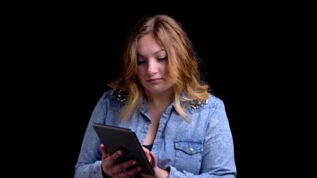 Nahauf-Porträt-von-erwachsenen-kaukasischen-weiblichen-Textnachrichten-auf-dem-Tablet-mit-Blick-auf-die-Kamera-und-lächelnd-mit-Hintergrund-isoliert-auf-schwarz