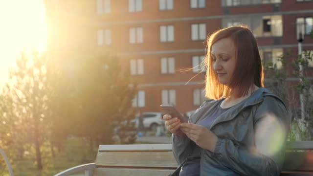 Woman-using-smartphone-sitting-on-bench-in-city