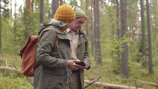 Senior-Paar-zu-Fuß-und-mit-Smartphone-in-Wald