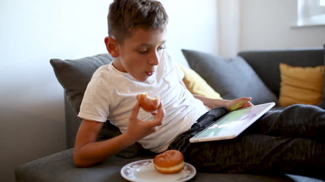 Junge-spielt-Spiele-auf-Tablet-und-essen-Donut